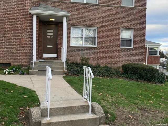 doorway to property featuring a lawn and brick siding