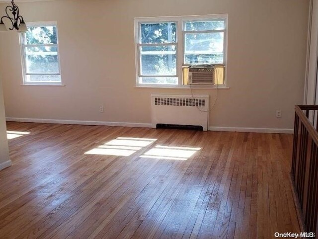 unfurnished room featuring radiator heating unit, hardwood / wood-style flooring, cooling unit, and a notable chandelier