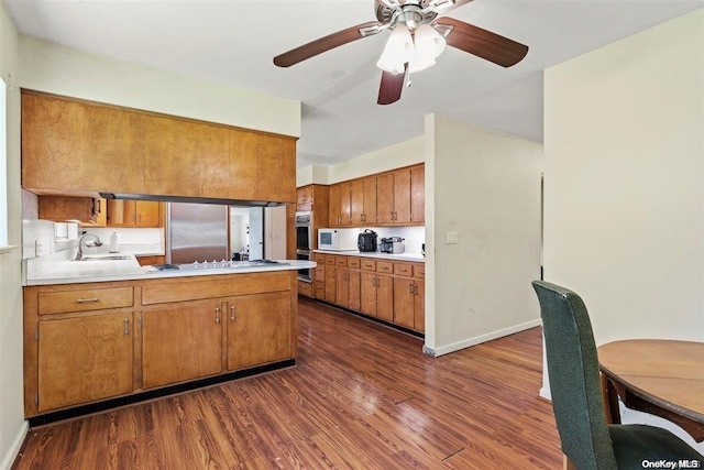 kitchen with kitchen peninsula, appliances with stainless steel finishes, ceiling fan, sink, and dark hardwood / wood-style floors