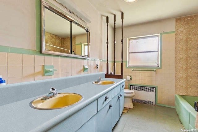 bathroom with vanity, radiator, a washtub, toilet, and tile walls