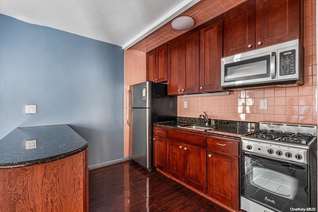 kitchen featuring sink, decorative backsplash, dark stone countertops, dark hardwood / wood-style flooring, and stainless steel appliances