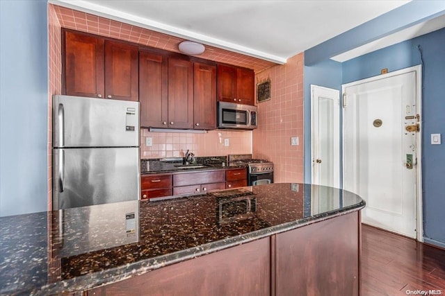 kitchen featuring sink, stainless steel appliances, dark hardwood / wood-style flooring, backsplash, and dark stone counters