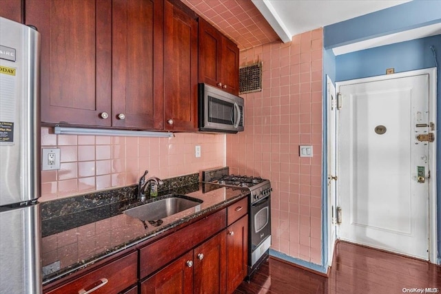 kitchen with dark stone counters, sink, tile walls, appliances with stainless steel finishes, and dark hardwood / wood-style flooring