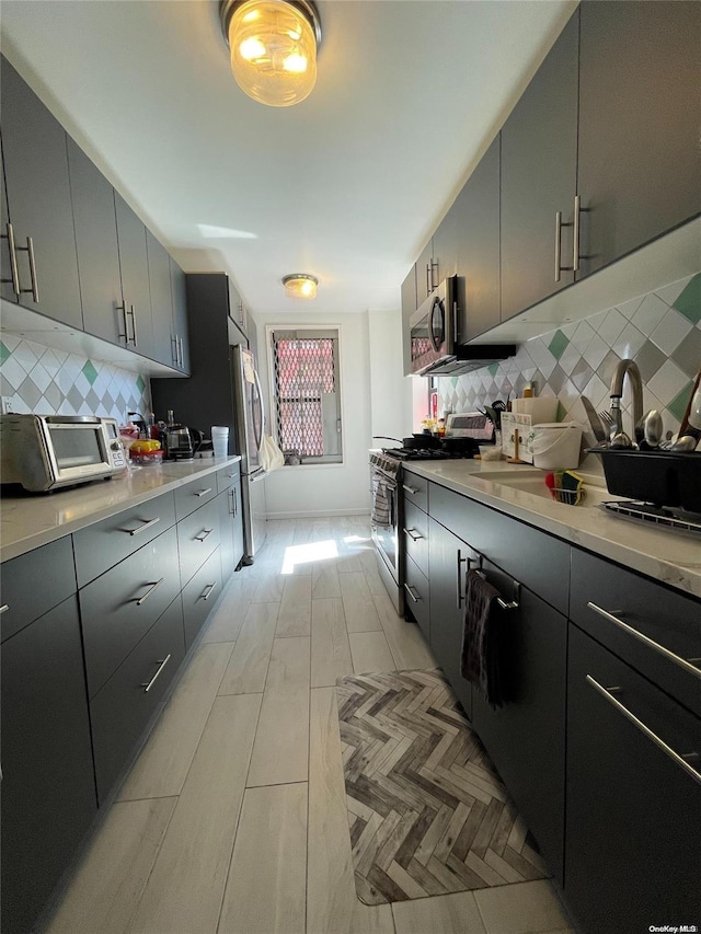 kitchen with gray cabinetry, sink, stainless steel appliances, and tasteful backsplash