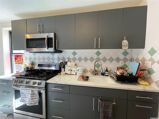 kitchen with sink, decorative backsplash, gray cabinets, light stone counters, and stainless steel appliances