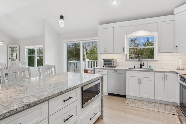 kitchen featuring pendant lighting, sink, vaulted ceiling, white cabinetry, and stainless steel appliances