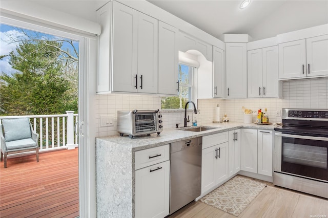 kitchen featuring sink, light hardwood / wood-style floors, vaulted ceiling, white cabinets, and appliances with stainless steel finishes