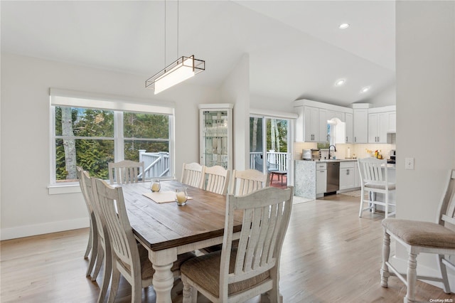 dining space featuring plenty of natural light, light hardwood / wood-style floors, sink, and high vaulted ceiling