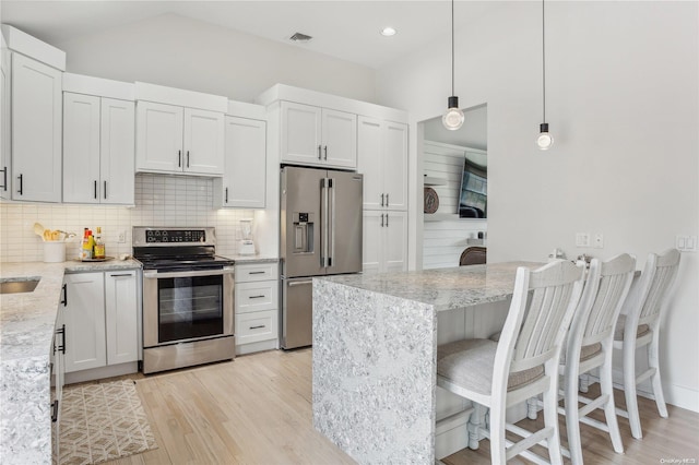 kitchen with white cabinets, stainless steel appliances, decorative light fixtures, and light hardwood / wood-style floors