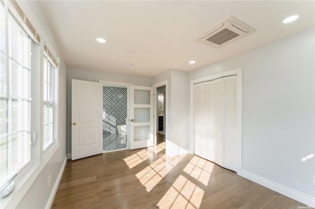 unfurnished bedroom with hardwood / wood-style floors, ensuite bath, and a closet