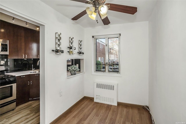 dining area with sink, radiator heating unit, ceiling fan, and light wood-type flooring