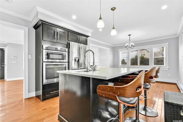 kitchen with a center island with sink, light wood-type flooring, stainless steel appliances, and hanging light fixtures