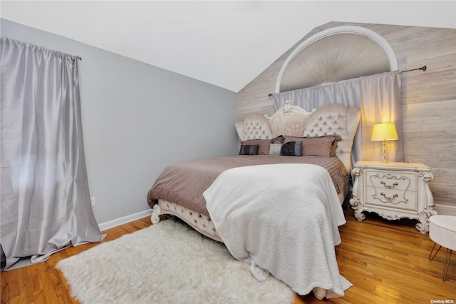 bedroom with wood-type flooring, lofted ceiling, and wooden walls