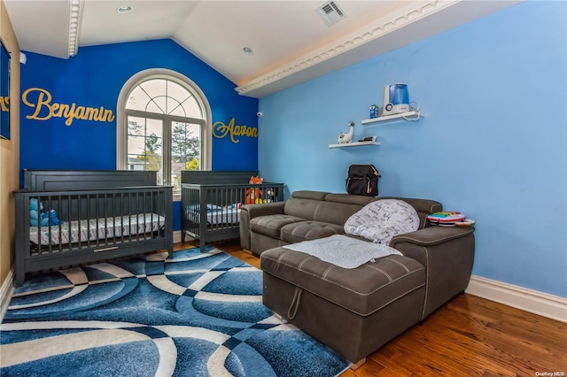 bedroom with lofted ceiling, a nursery area, and dark hardwood / wood-style floors