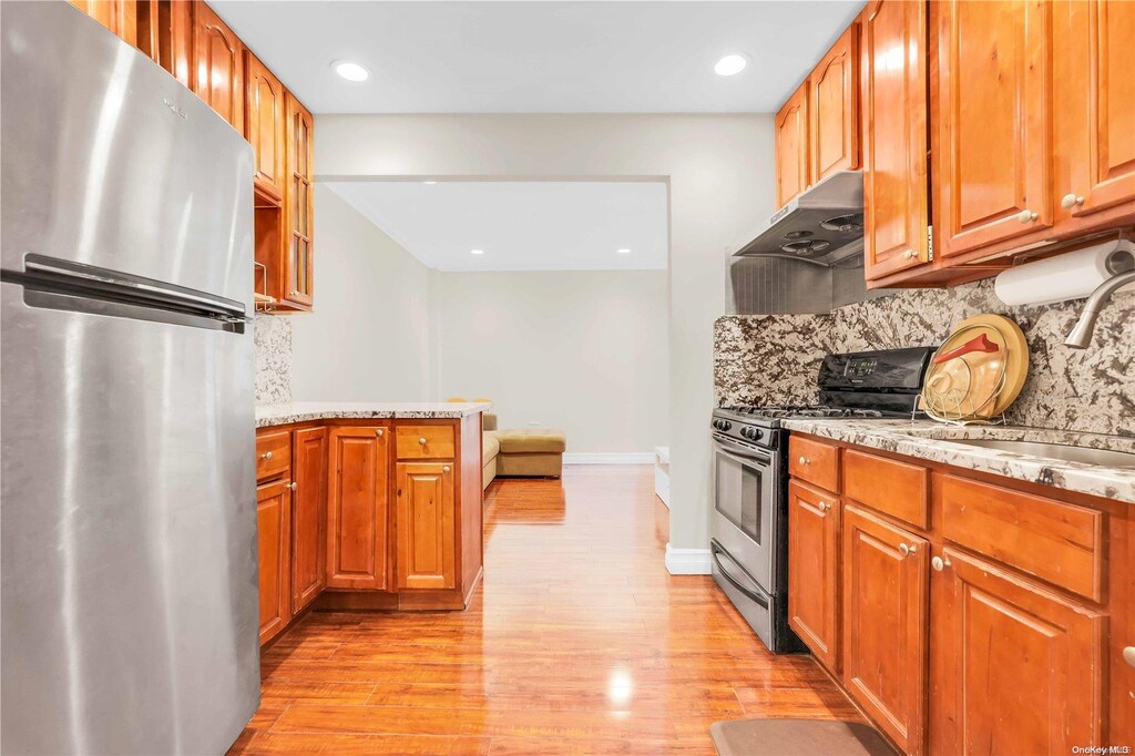 kitchen with backsplash, light stone counters, light hardwood / wood-style flooring, and stainless steel appliances