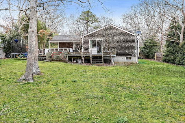 back of property with a lawn, a deck, and a trampoline