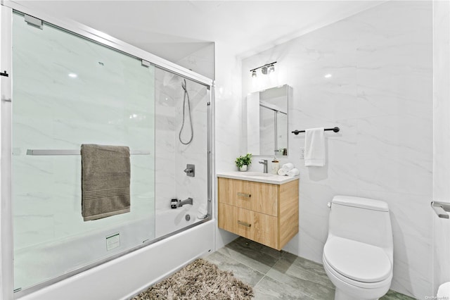 full bathroom featuring shower / bath combination with glass door, vanity, toilet, and tile walls