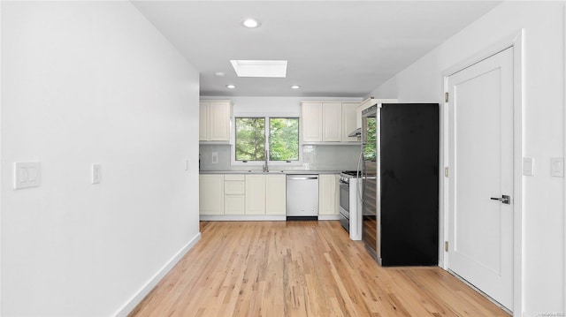 kitchen featuring backsplash, sink, a skylight, appliances with stainless steel finishes, and light hardwood / wood-style floors