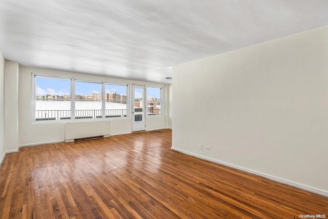 empty room featuring radiator heating unit, a water view, and wood-type flooring