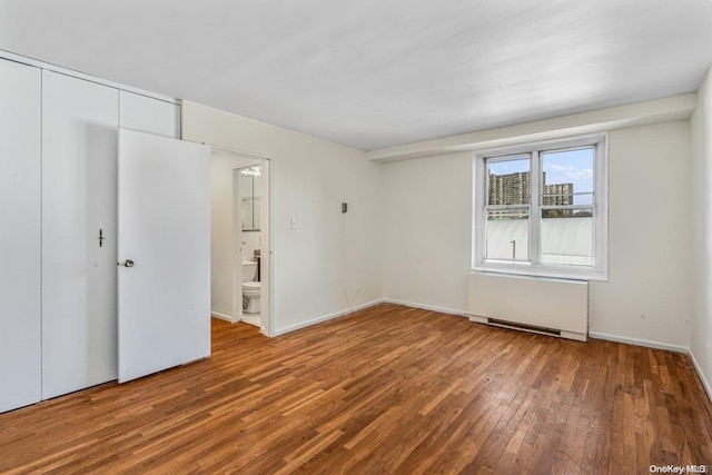 unfurnished bedroom featuring connected bathroom, hardwood / wood-style floors, and radiator heating unit