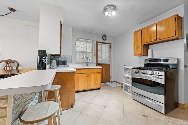 kitchen with kitchen peninsula, appliances with stainless steel finishes, decorative backsplash, sink, and light tile patterned floors