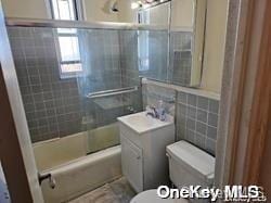 full bathroom featuring vanity, toilet, tile walls, and bath / shower combo with glass door