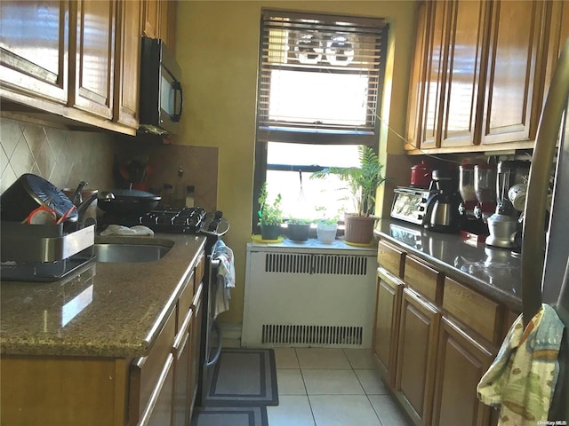 kitchen with backsplash, radiator heating unit, light tile patterned floors, and dark stone counters