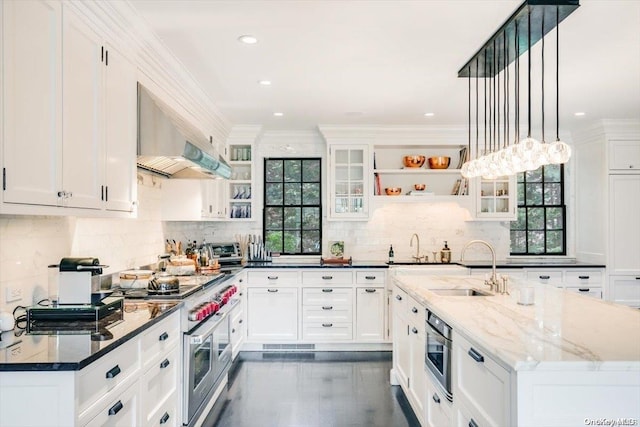 kitchen with dark stone counters, wall chimney exhaust hood, stainless steel appliances, crown molding, and pendant lighting