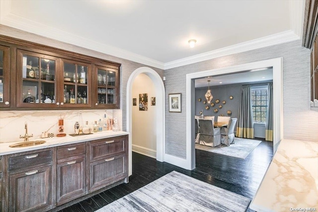 bar featuring dark wood-type flooring, crown molding, sink, hanging light fixtures, and light stone countertops