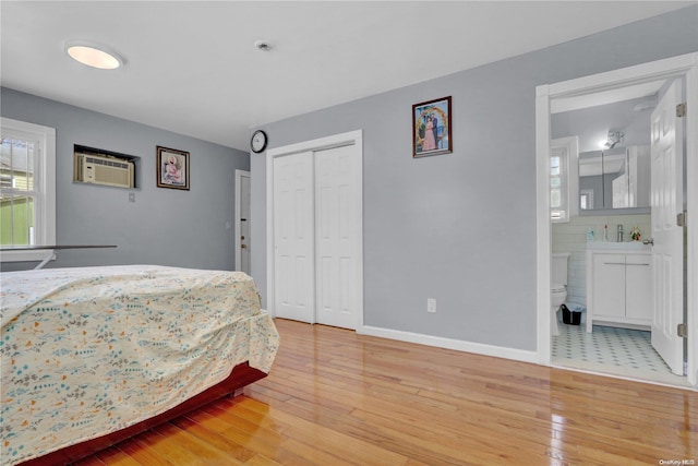 bedroom featuring a wall mounted air conditioner, a closet, wood-type flooring, and ensuite bath