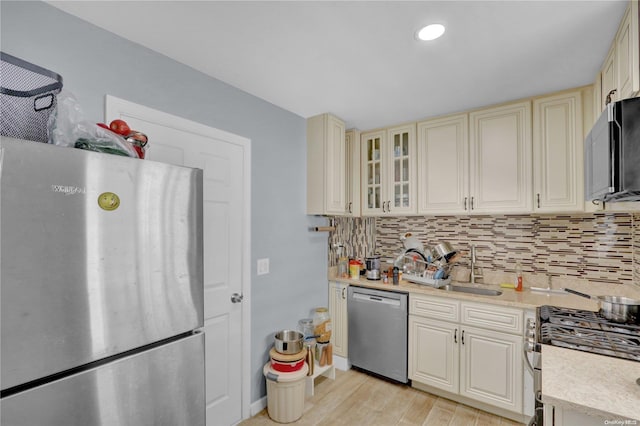 kitchen featuring sink, backsplash, cream cabinetry, appliances with stainless steel finishes, and light wood-type flooring