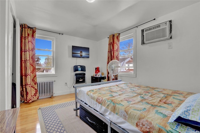 bedroom with a wall mounted air conditioner, hardwood / wood-style floors, and radiator