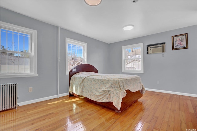 bedroom with multiple windows, radiator heating unit, light hardwood / wood-style floors, and a wall mounted AC