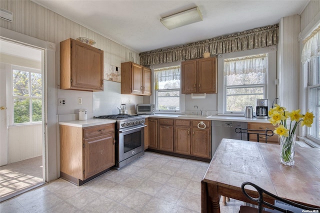 12115 Main Rd, East Marion, NY 11939 - kitchen featuring appliances with stainless steel finishes, a sink, healthy amount of natural light, brown cabinets, and wood walls