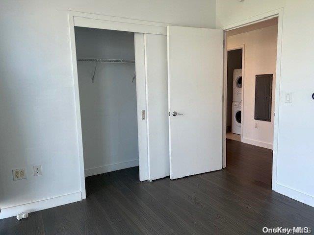 unfurnished bedroom featuring stacked washer / drying machine, dark hardwood / wood-style floors, electric panel, and a closet