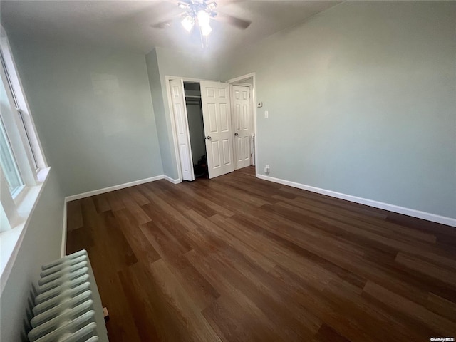 unfurnished bedroom with ceiling fan, radiator heating unit, dark wood-type flooring, and a closet