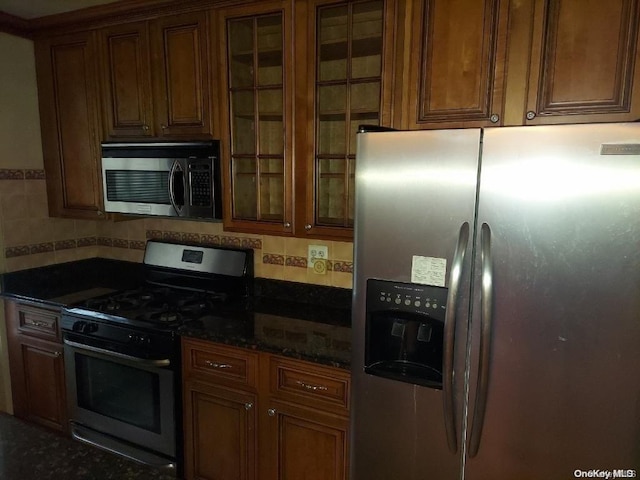 kitchen featuring decorative backsplash, appliances with stainless steel finishes, and dark stone countertops