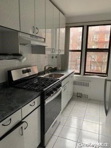 kitchen featuring light tile patterned flooring, sink, radiator heating unit, gas stove, and white cabinetry