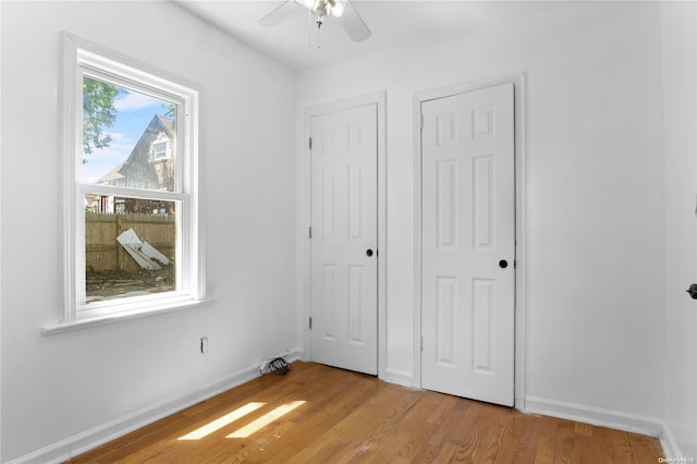 unfurnished bedroom with ceiling fan, light wood-type flooring, and multiple closets