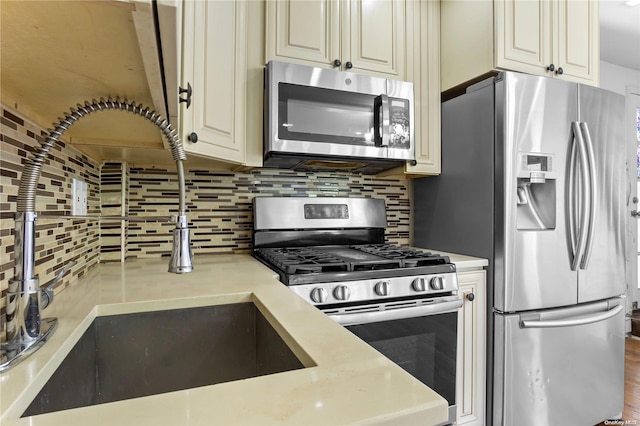 kitchen featuring hardwood / wood-style floors, cream cabinets, sink, decorative backsplash, and appliances with stainless steel finishes