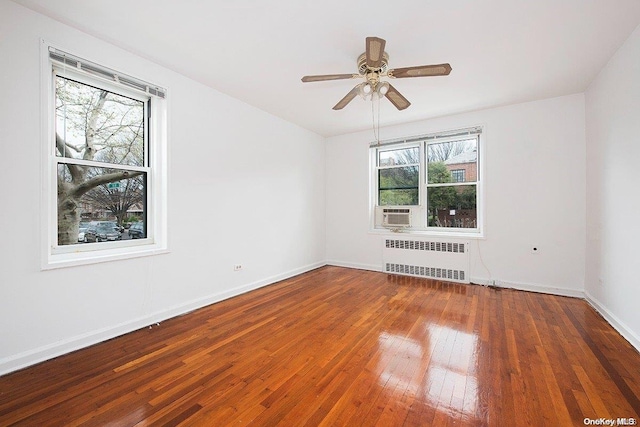 unfurnished room with a wealth of natural light, dark hardwood / wood-style floors, radiator, and ceiling fan