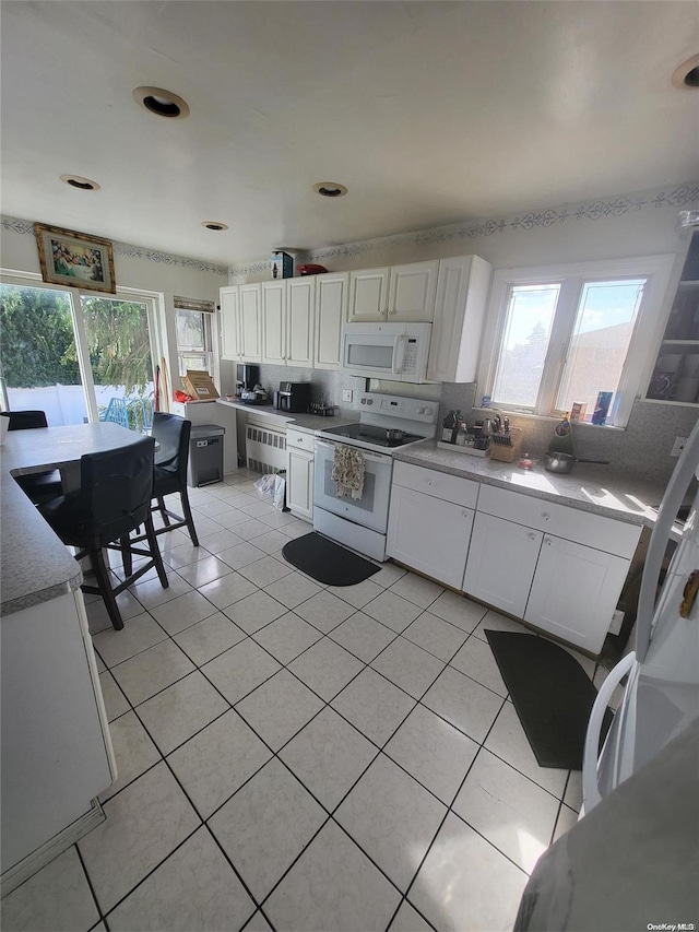 kitchen featuring light tile patterned floors, white appliances, white cabinetry, and radiator heating unit