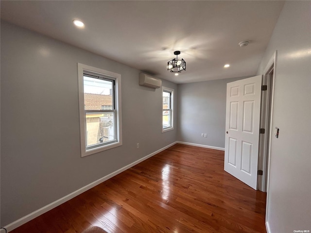 empty room featuring dark hardwood / wood-style flooring, a wall unit AC, and an inviting chandelier