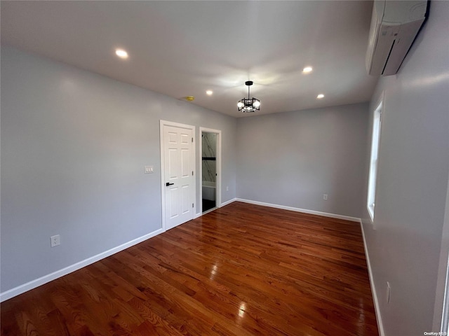 spare room featuring an AC wall unit, a chandelier, and dark wood-type flooring