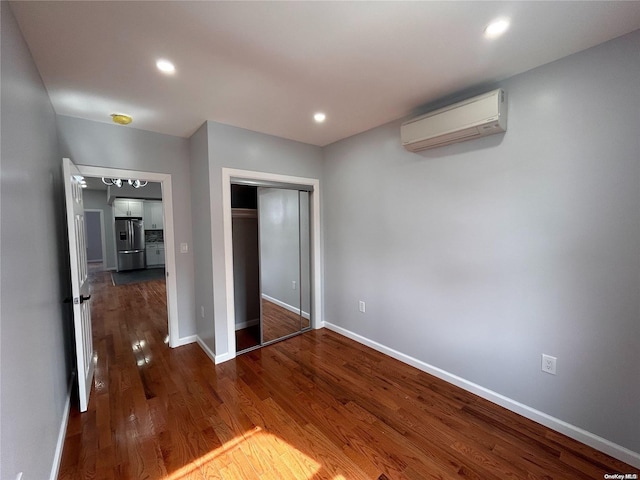 unfurnished bedroom with stainless steel refrigerator with ice dispenser, an AC wall unit, a closet, and dark wood-type flooring