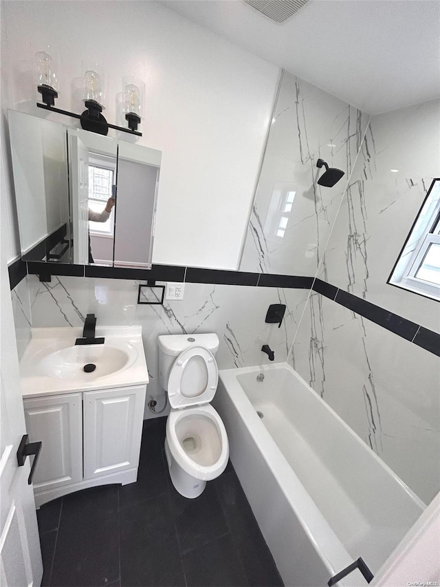 full bathroom with vanity, tiled shower / bath combo, tile walls, tile patterned flooring, and toilet