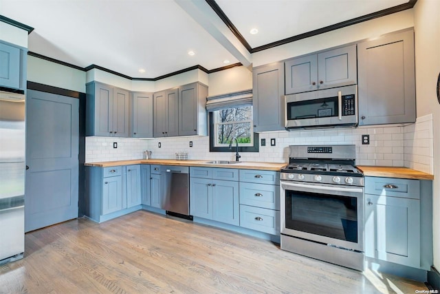 kitchen with appliances with stainless steel finishes, light wood-type flooring, crown molding, sink, and butcher block counters