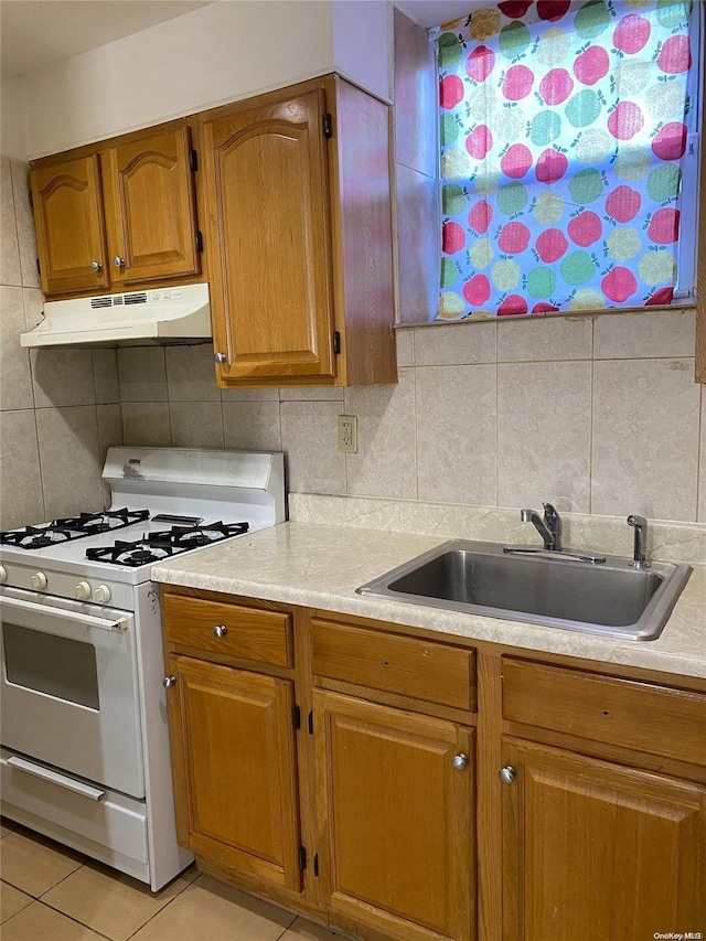 kitchen with tasteful backsplash, sink, light tile patterned floors, and white gas range oven