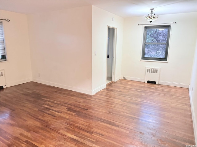 unfurnished room with hardwood / wood-style flooring, radiator heating unit, and an inviting chandelier