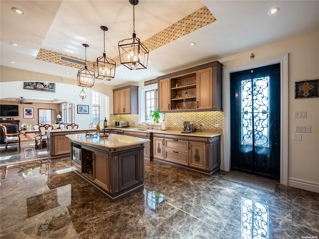 kitchen featuring ceiling fan, pendant lighting, a tray ceiling, decorative backsplash, and a center island with sink